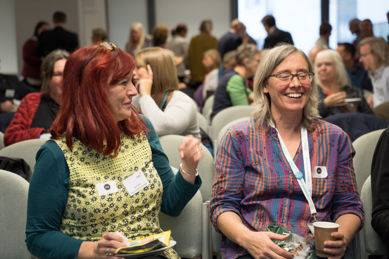 Two people at a meeting laugh together whilst having a cup of tea