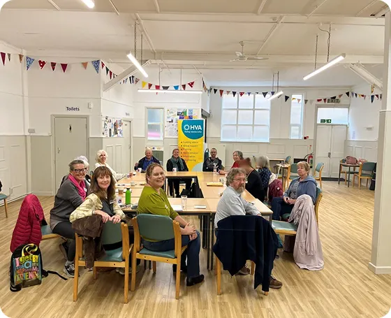 A group of people from the community sitting around a table in Central Hall, with some HVA staff, all looking towards the camera
