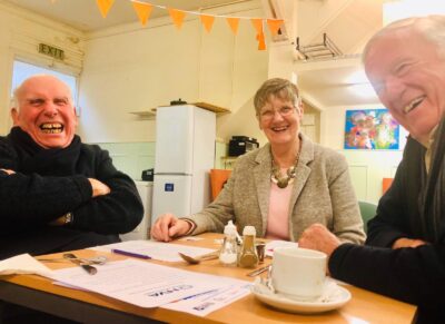 Three older people sat at a meeting table smiling