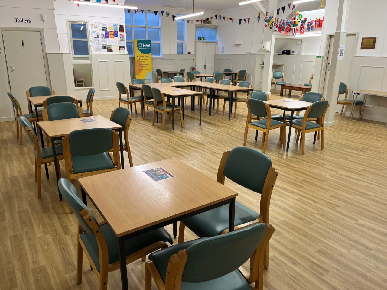 Central hall with several tables and chairs set out. There is bunting hung up and a leaflet on each table