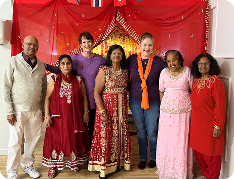 Two HVA members standing with a group of community members, all dressed up in their finery and posing for a photo in front of curtains
