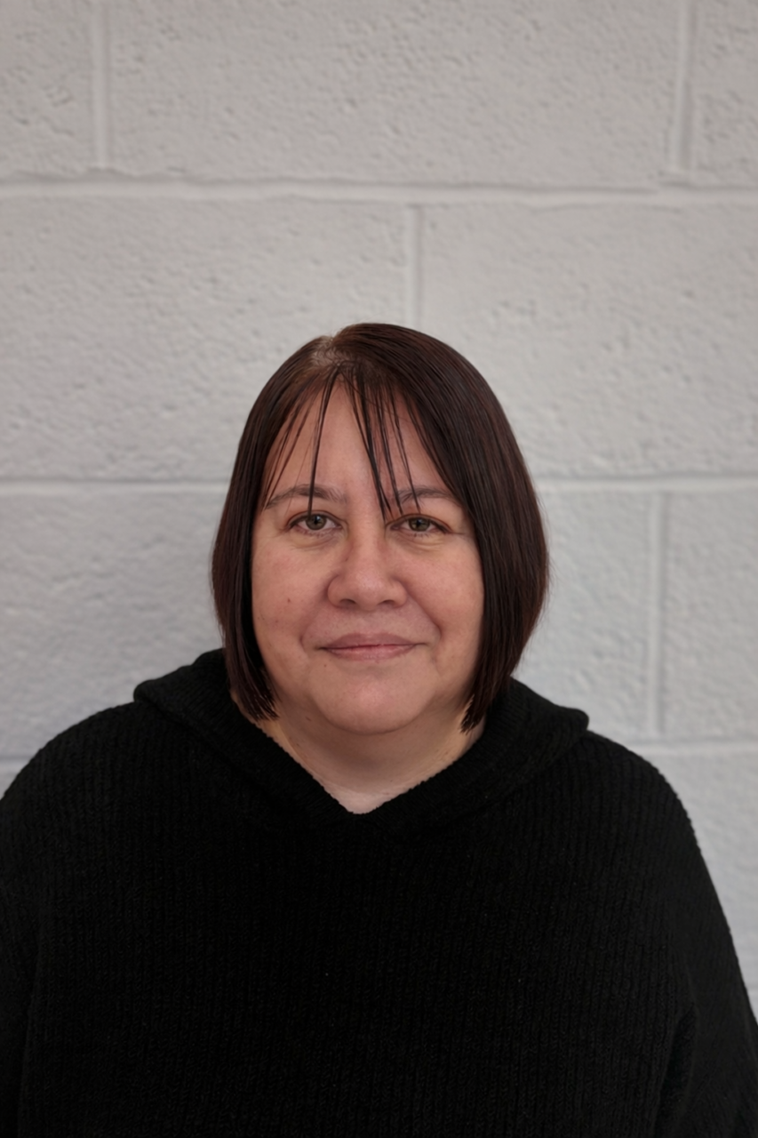 Angie Lowe sitting against a white brick wall, smiling at the camera