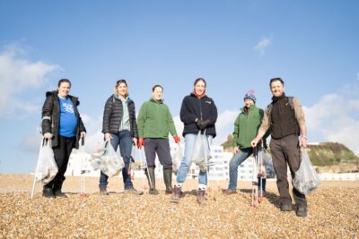 6 people involved in a beach clean in Hastings. They are standing on shingle and there is blue sky behind them.