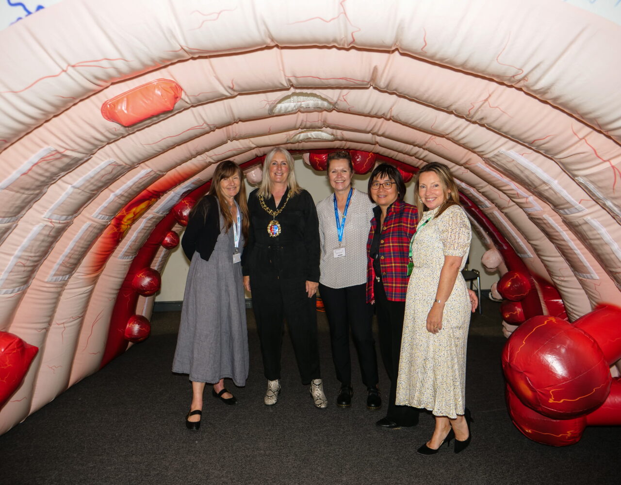 Large-scale inflatable bowel with The Mayor of Hastings, Cllr Paula Warne, Mary Carter, Chair of HVA, Emma Banfield and Wen Chiu of the Sussex and Surrey bowel screening team, and Jane Dodson standing inside the inflatable bowel.